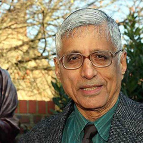 A man wearing glasses and a suit and tie is smiling for the camera.