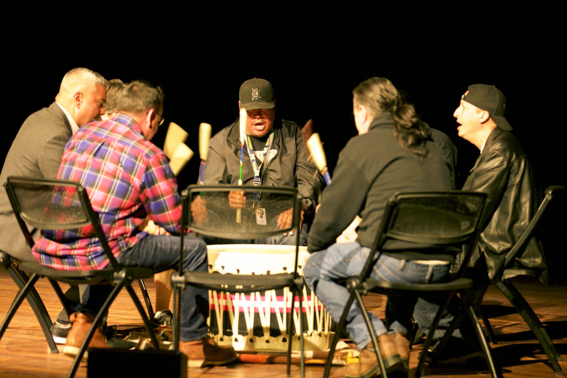 A group of men are sitting around a drum in a dark room.