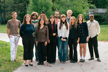 Group of people standing outside on a path, with trees in the background. Some are smiling.