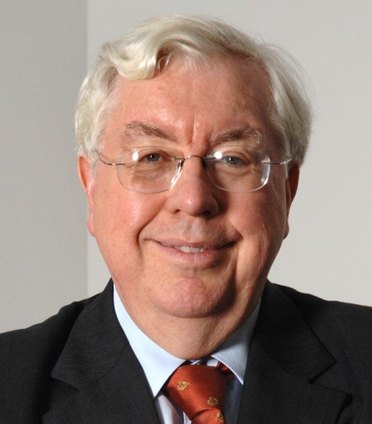 A man wearing glasses and a suit smiles for the camera