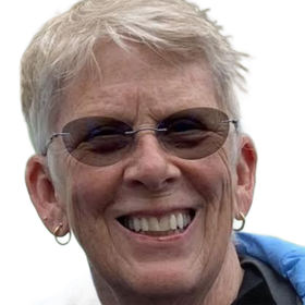 Smiling person wearing sunglasses and a blue jacket in front of a waterfall