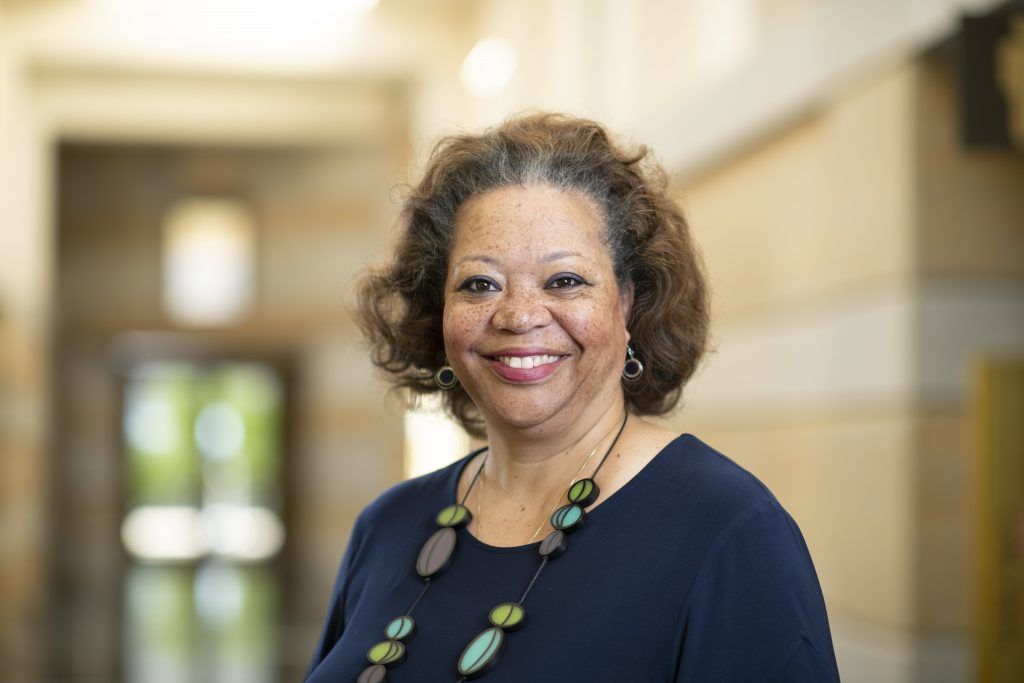 A woman wearing a blue shirt and a necklace is smiling for the camera.