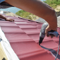 A person is using a drill on a red roof.