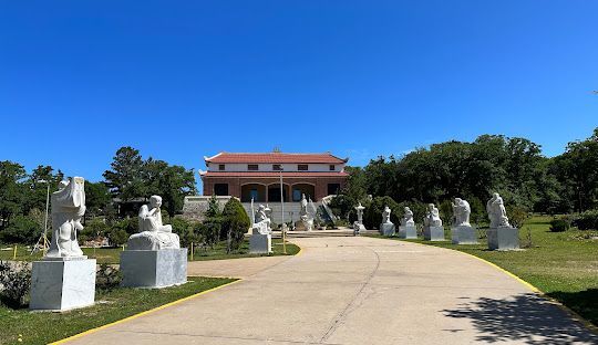 There are many statues on the side of the road in front of a building.