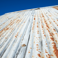 Looking up at a rusty metal roof with a blue sky in the background