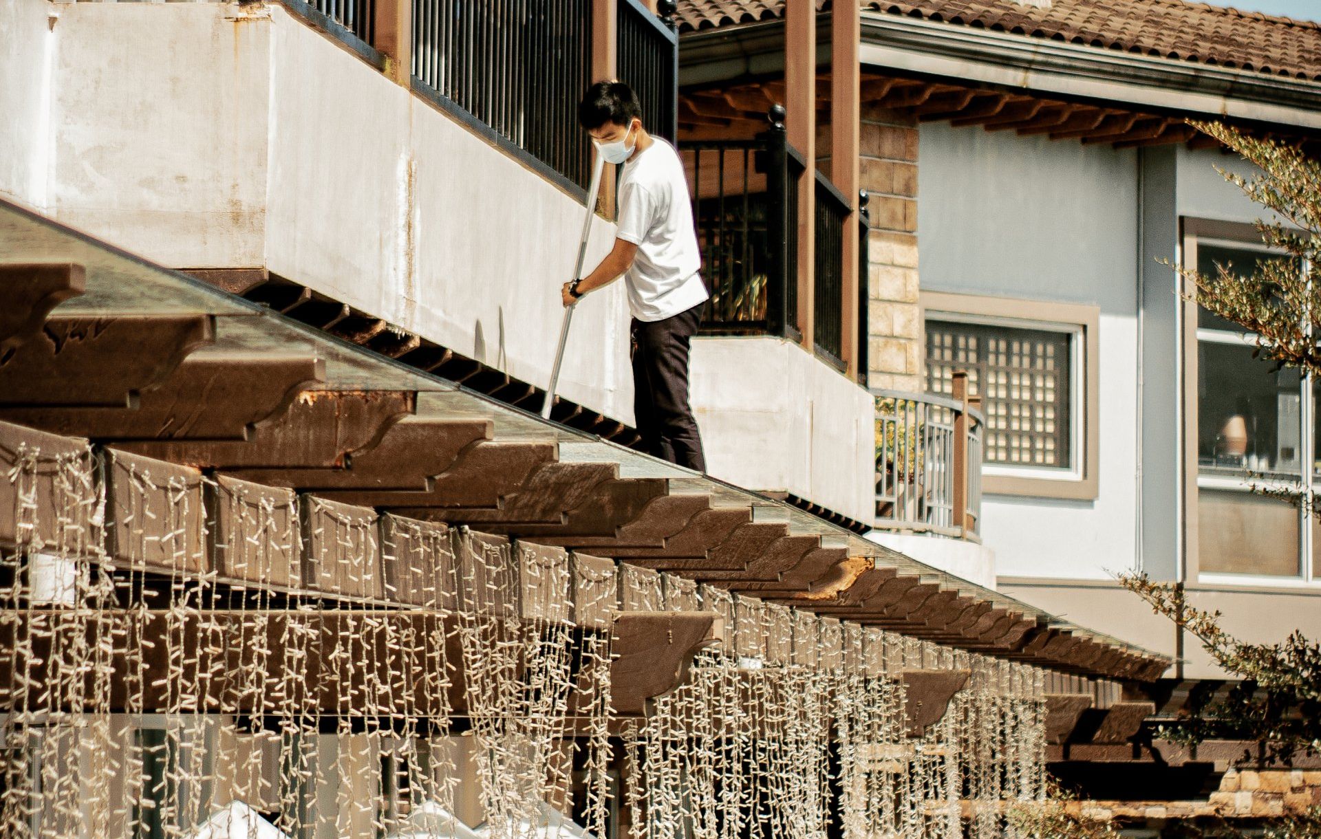 A man wearing a mask is standing on a balcony holding a broom.