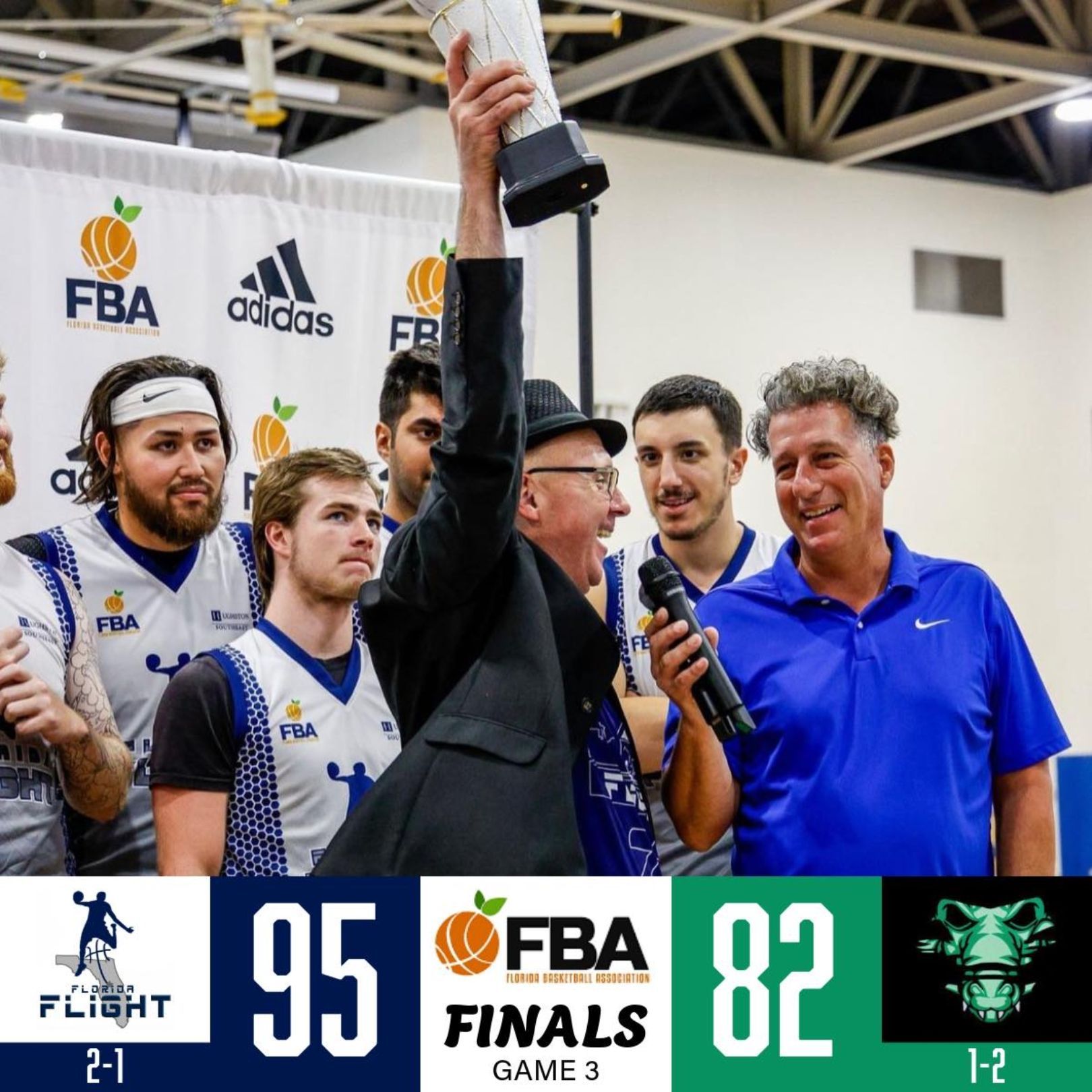 A man holding a trophy in front of a scoreboard that says 95-82