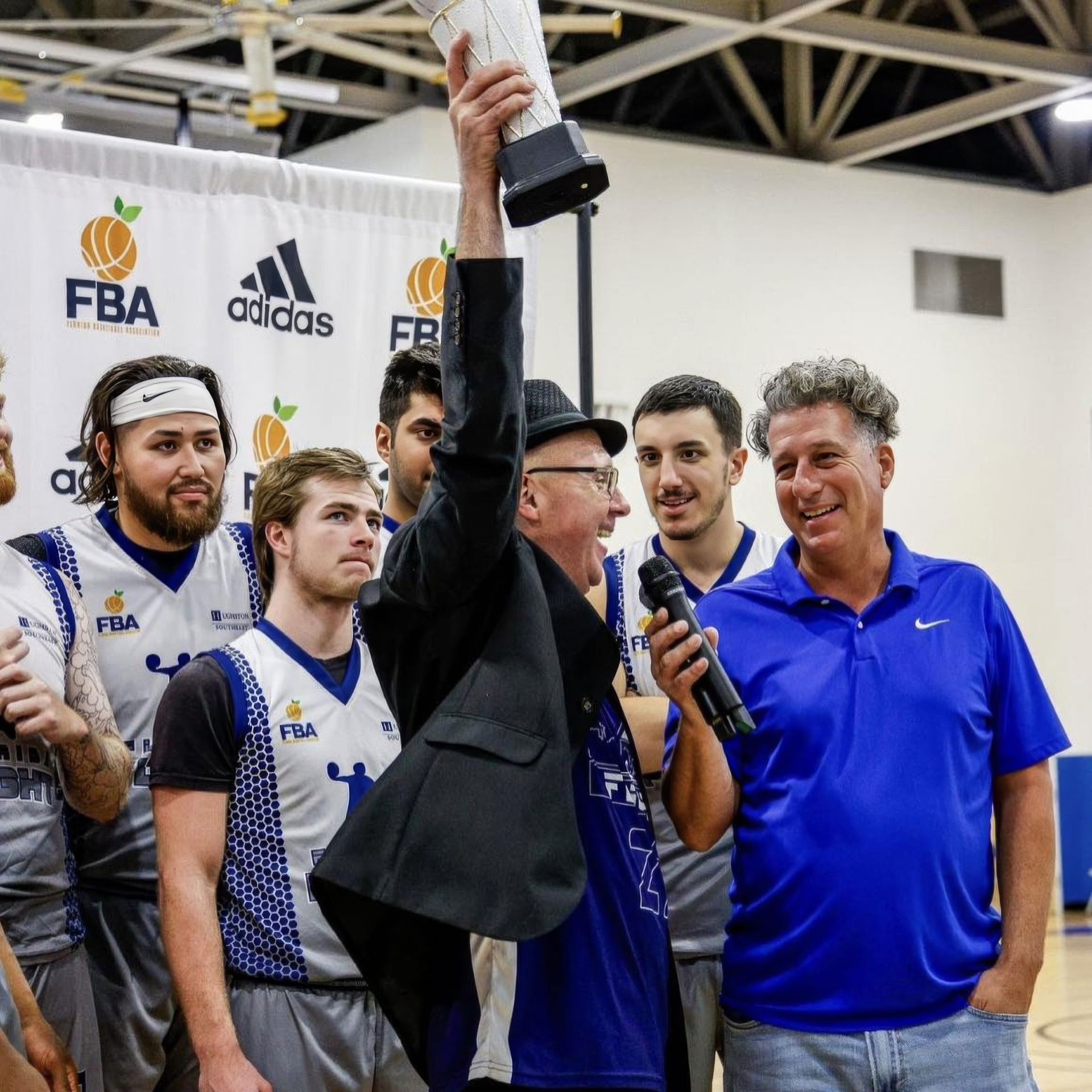 A man is holding up a trophy in front of a group of basketball players