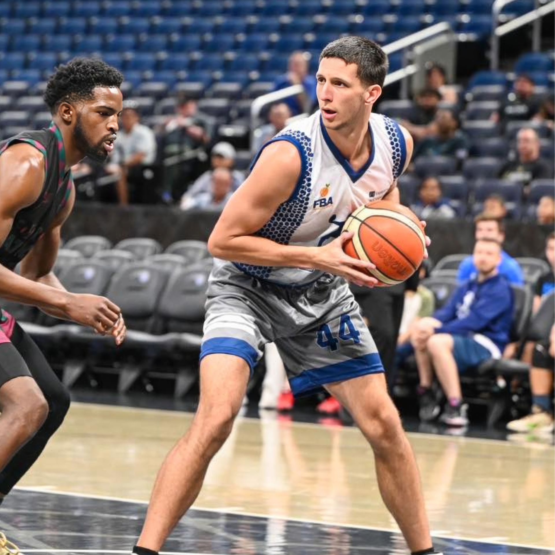 Two basketball players are playing a game of basketball on a court.