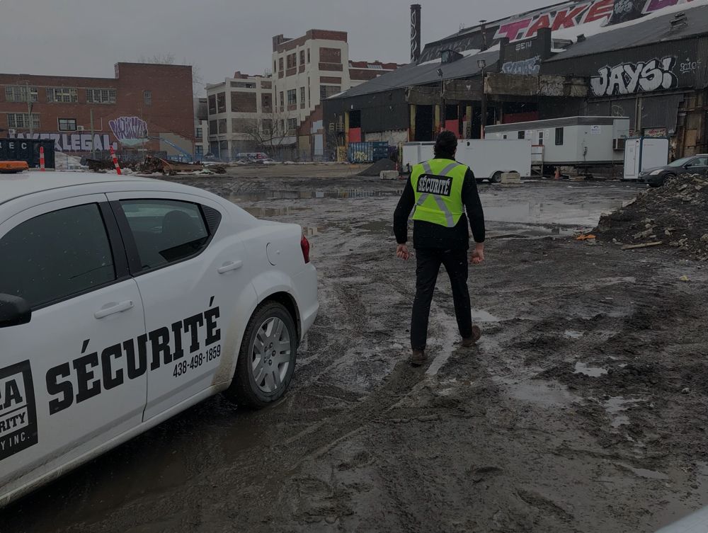 Un homme portant un gilet jaune se tient à côté d'une voiture blanche sur laquelle est écrit « sécurité ».