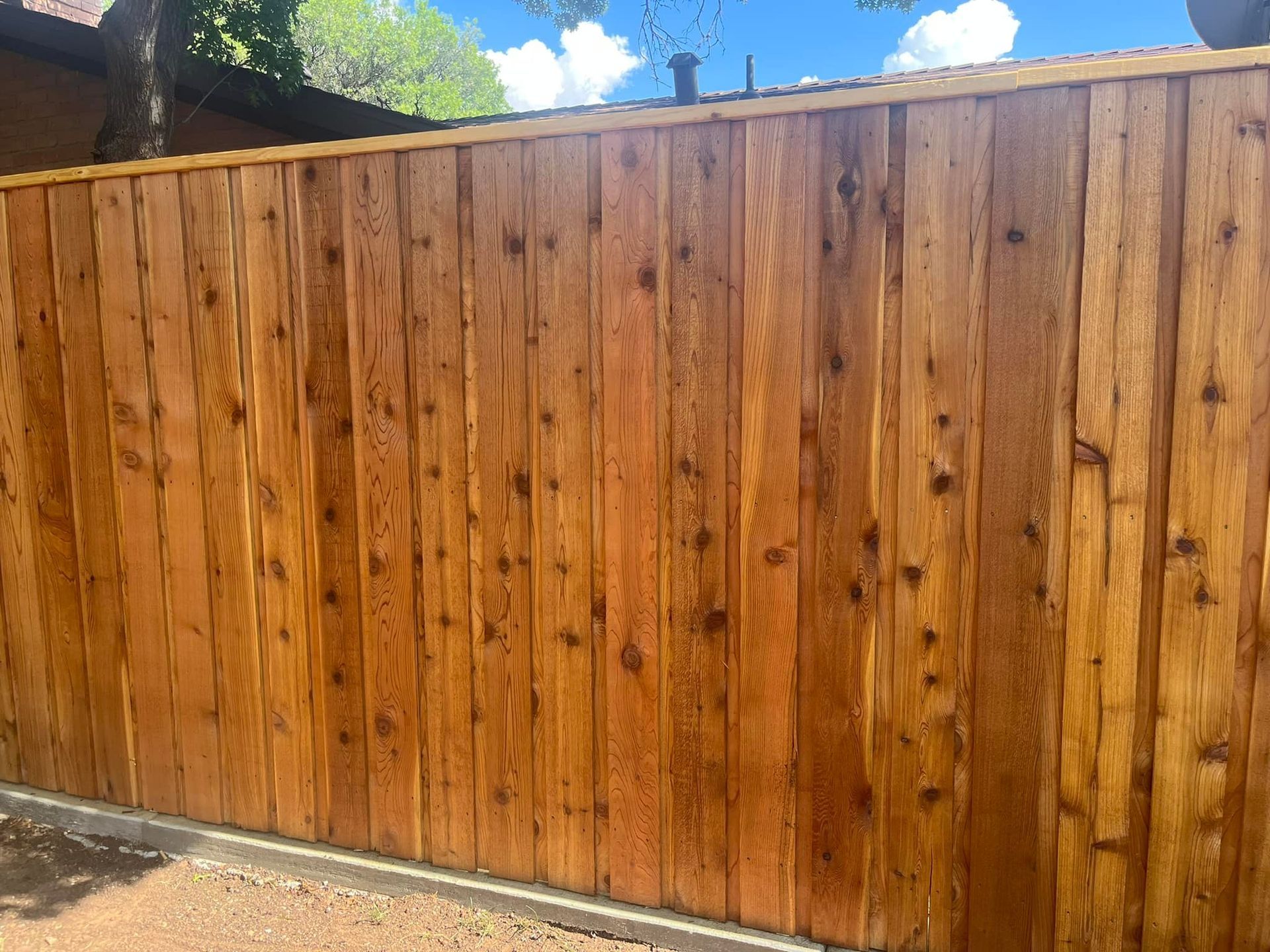 Wooden privacy fence, stained brown, with a row of concrete edging below and a clear sky above.