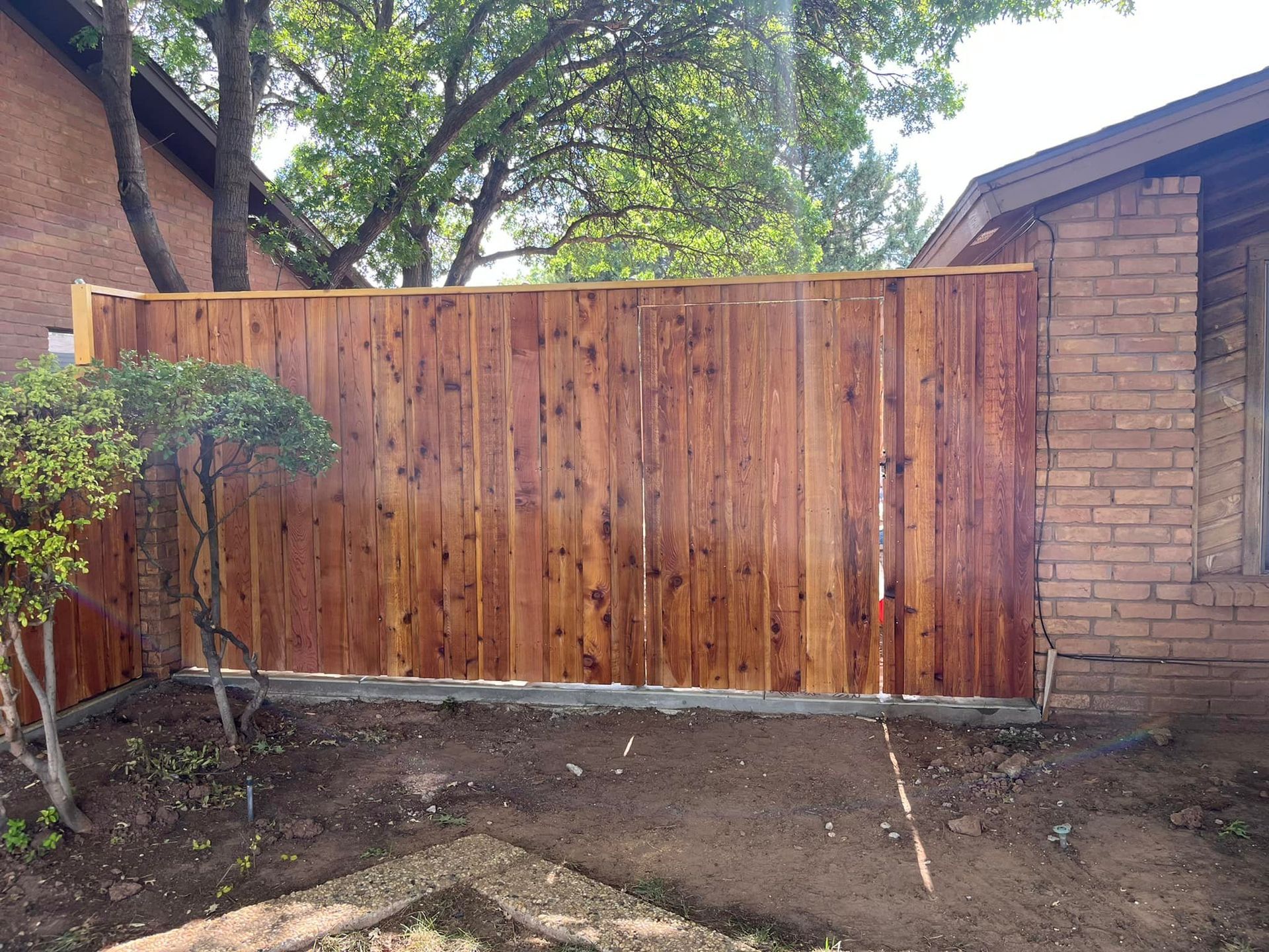 Wooden fence next to a brick building and a small bush in a yard.
