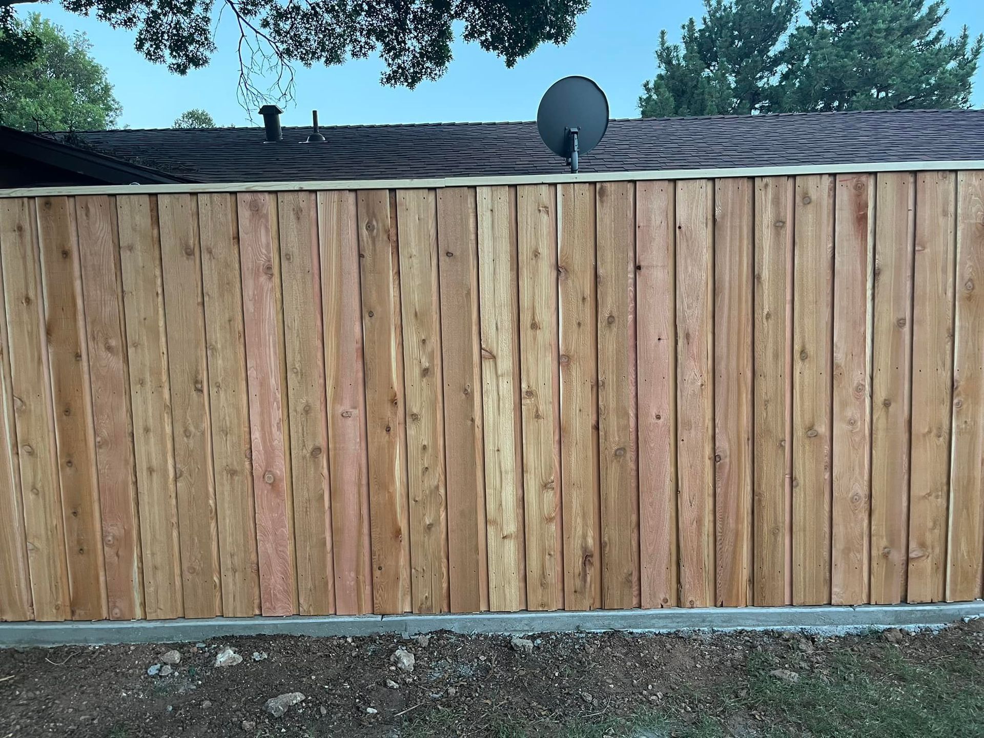 Wooden fence in front of a house; brown planks; satellite dish on the roof.