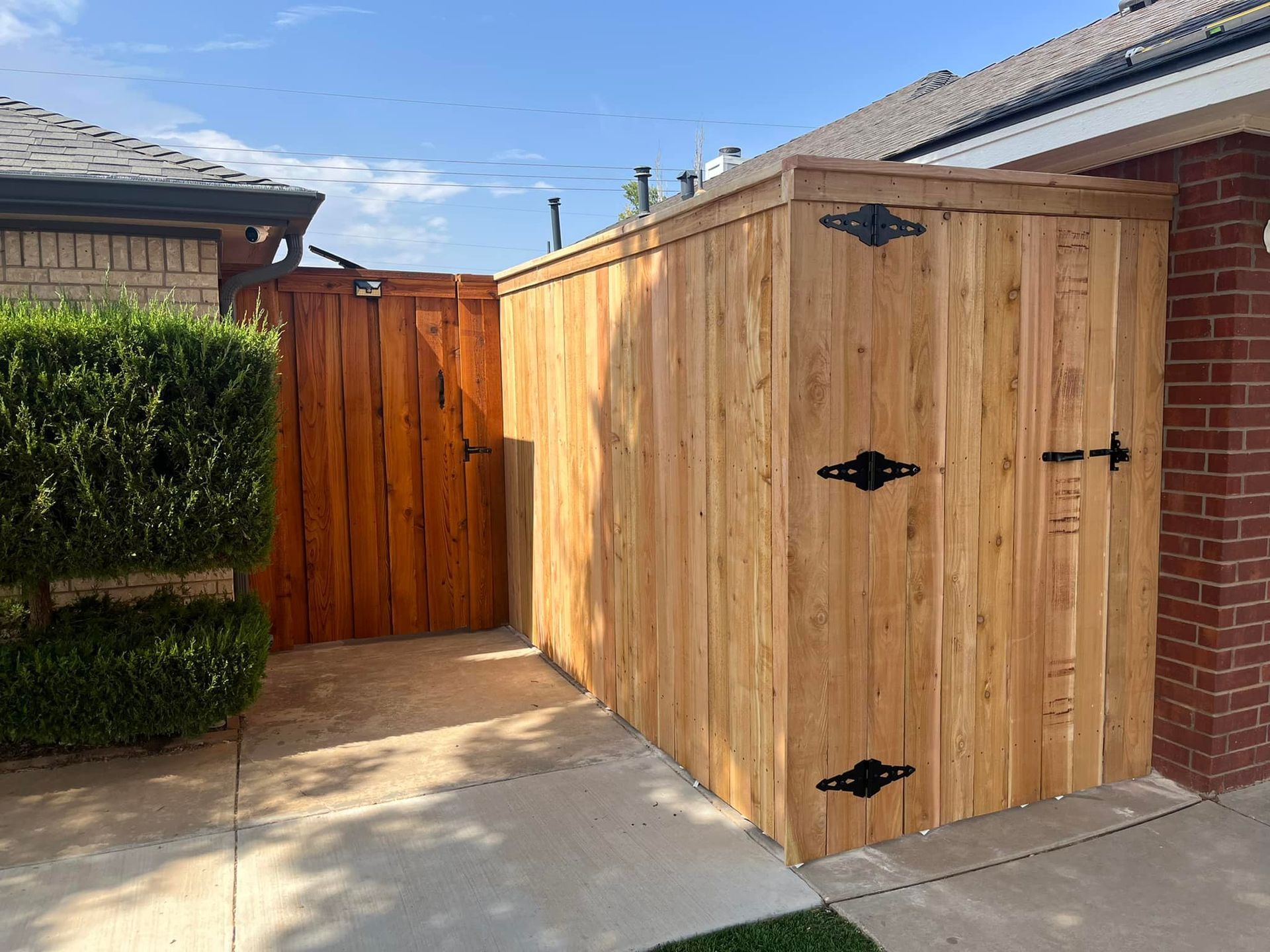 Wooden storage shed and gate, adjacent to a brick house, on a concrete driveway.