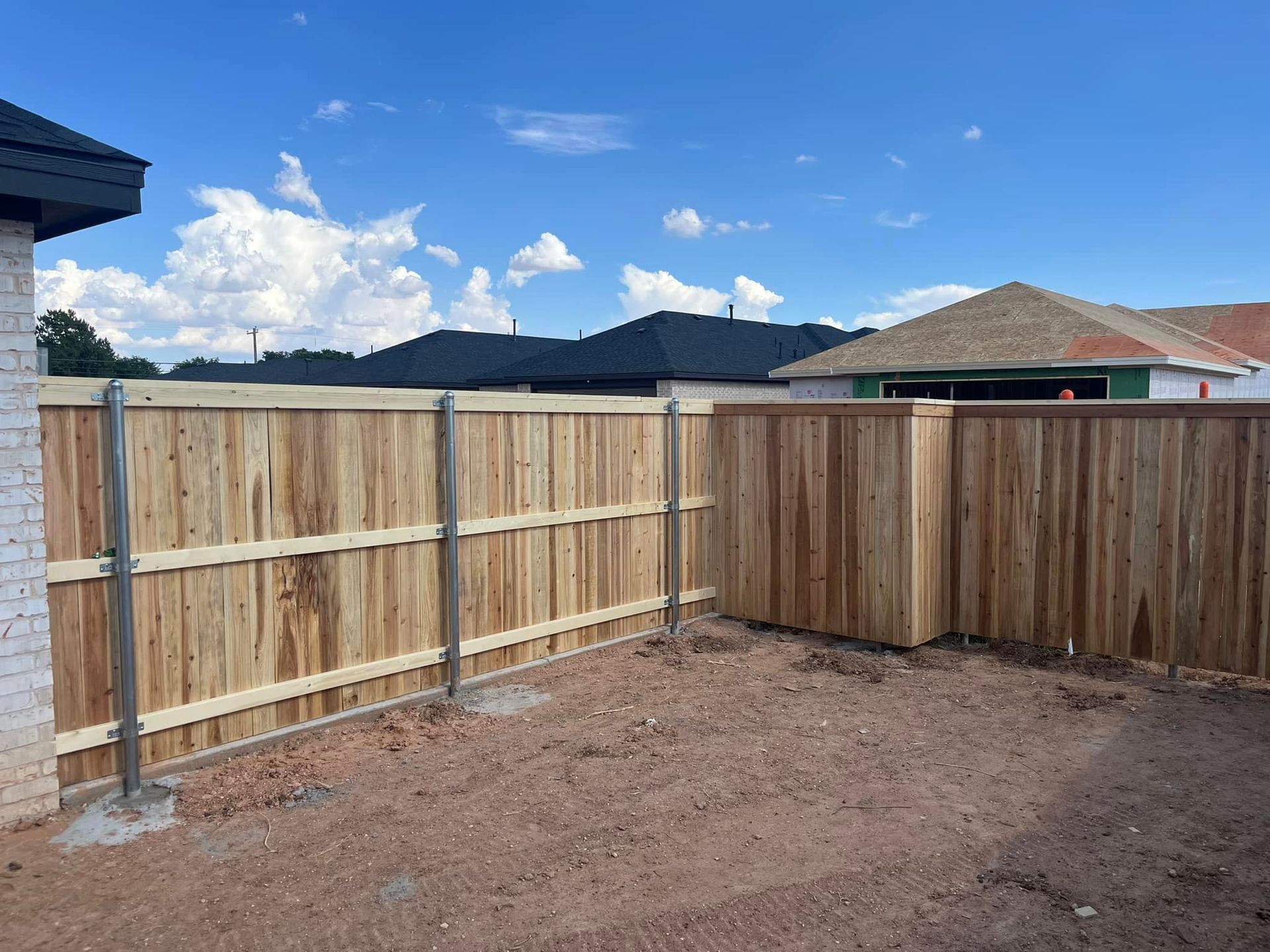 Wooden fence surrounding a yard, against a blue sky with some houses in the background.