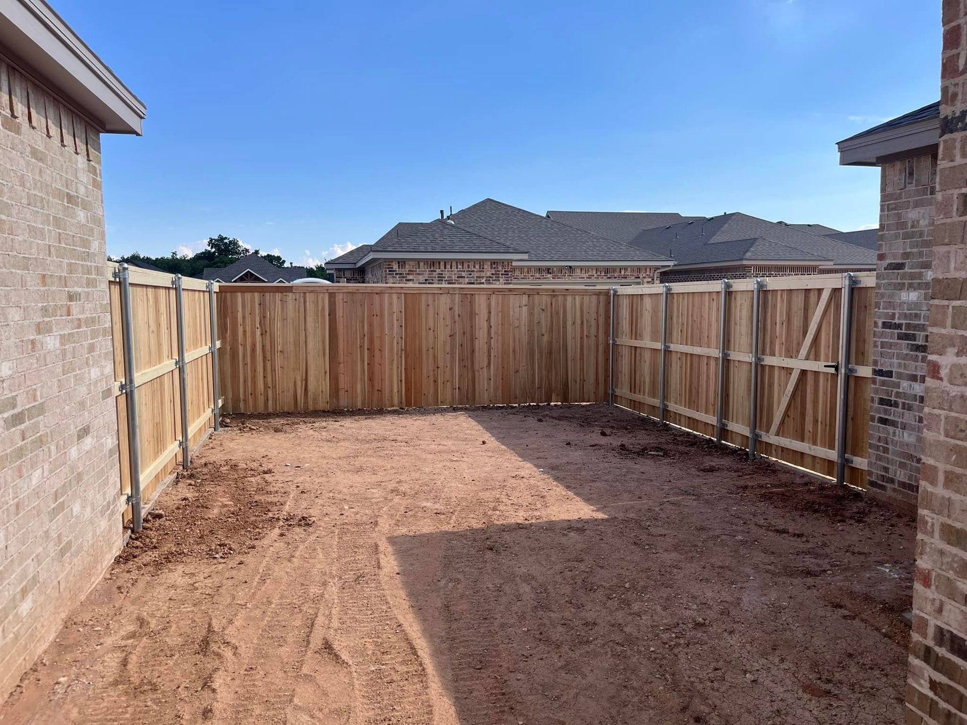 Backyard enclosed by a wooden fence and brick walls, under a clear blue sky.