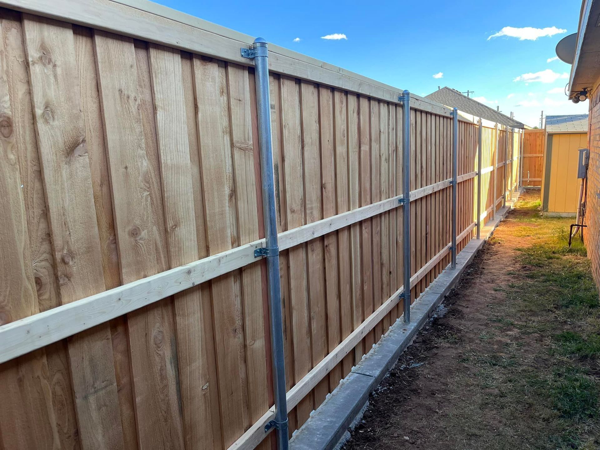 Wooden fence with metal posts in a yard, under a blue sky.
