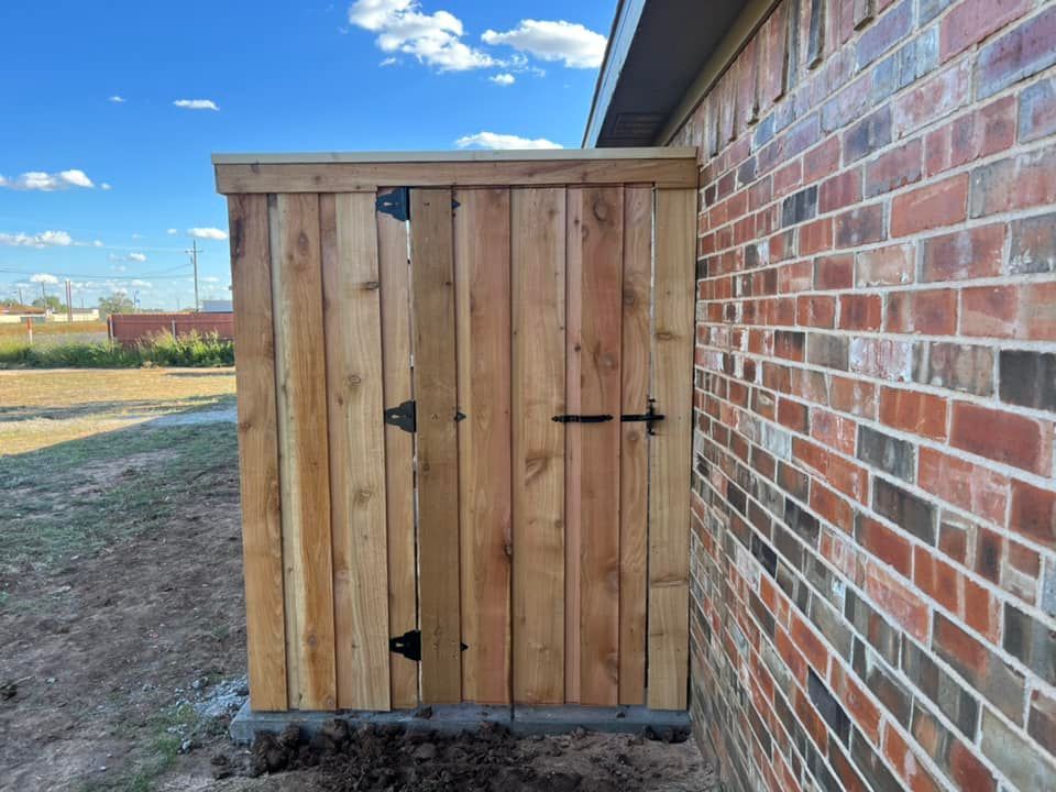 Wooden storage shed built against a red brick wall. The shed is secured with a latch and hinges.