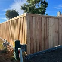 Wooden fence against a blue sky with trees.