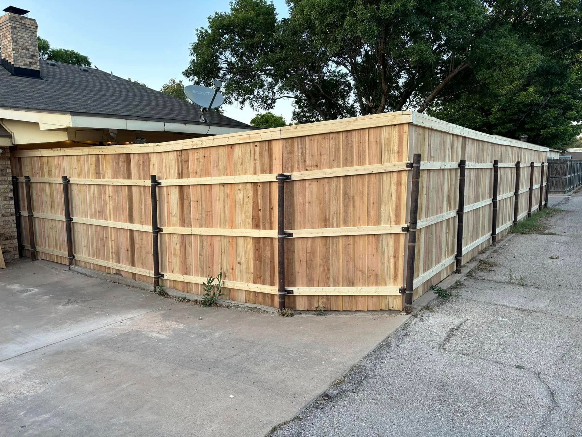 Wooden privacy fence along a concrete driveway next to a house with a dark roof.