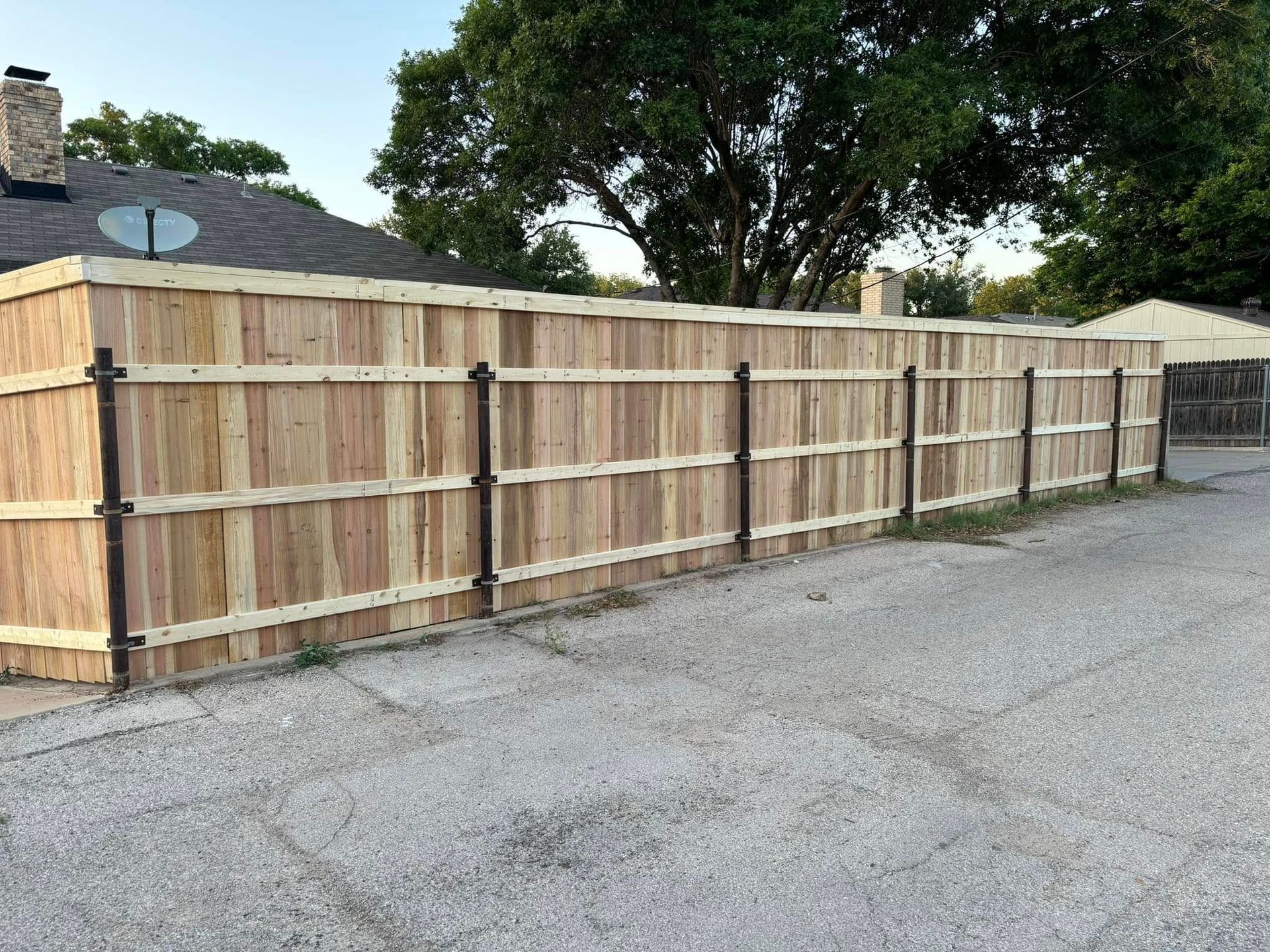Wooden fence bordering a gravel area; brown, vertical boards, dark metal posts.