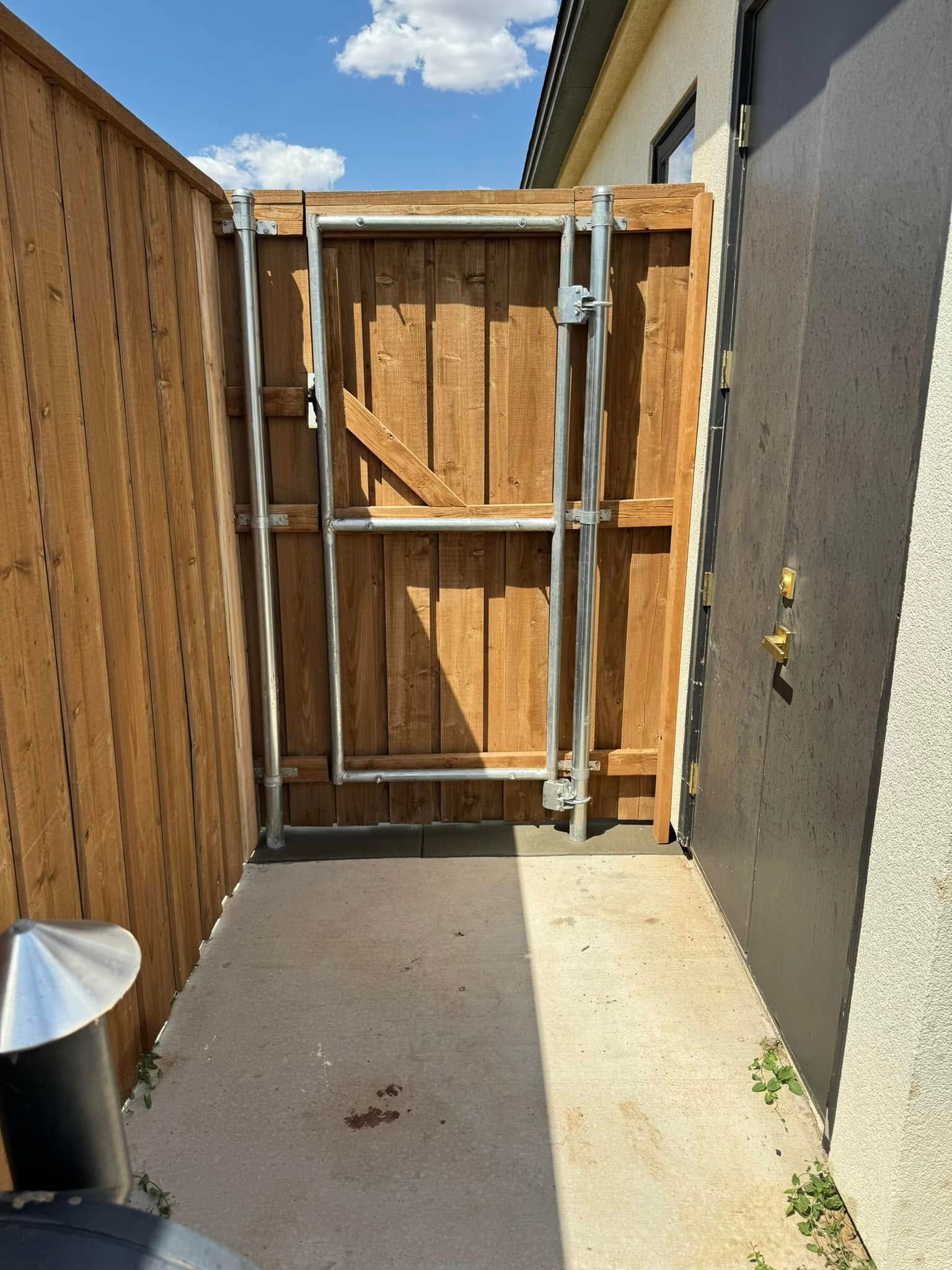 Wooden gate in a narrow passage between a wooden fence and a dark wall, concrete floor.