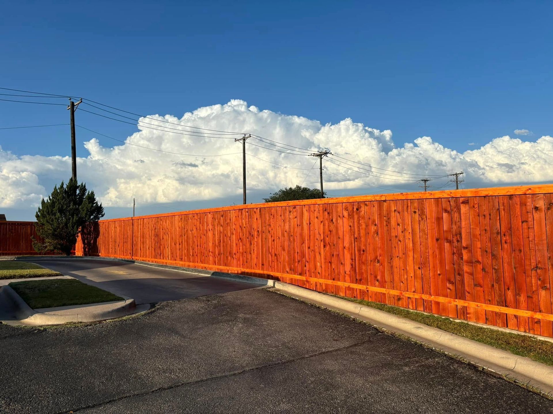 Orange wooden fence in front of a cloudy sky, with telephone poles and road visible.