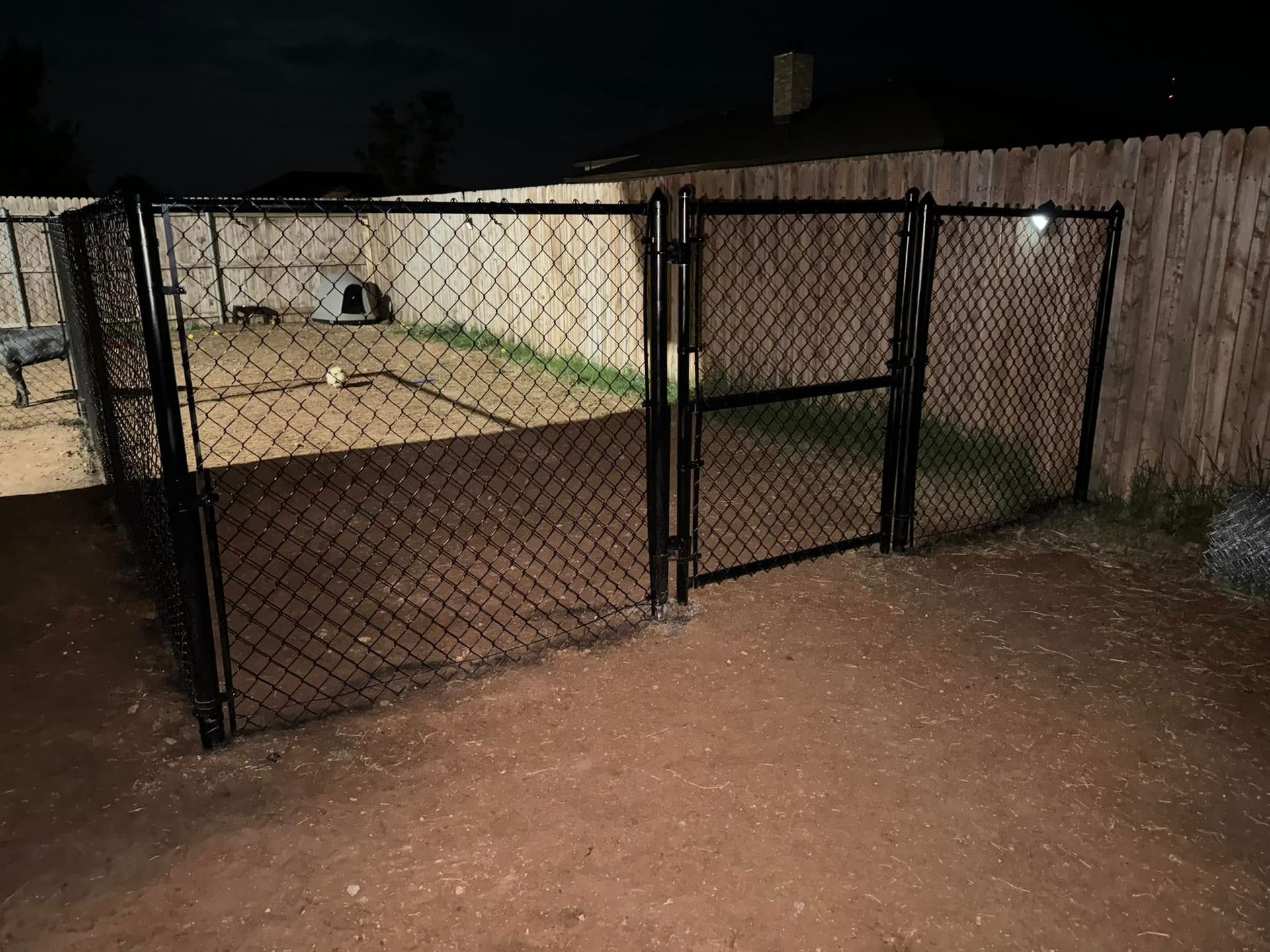 Black chain-link fence with three gates in a backyard; nighttime.