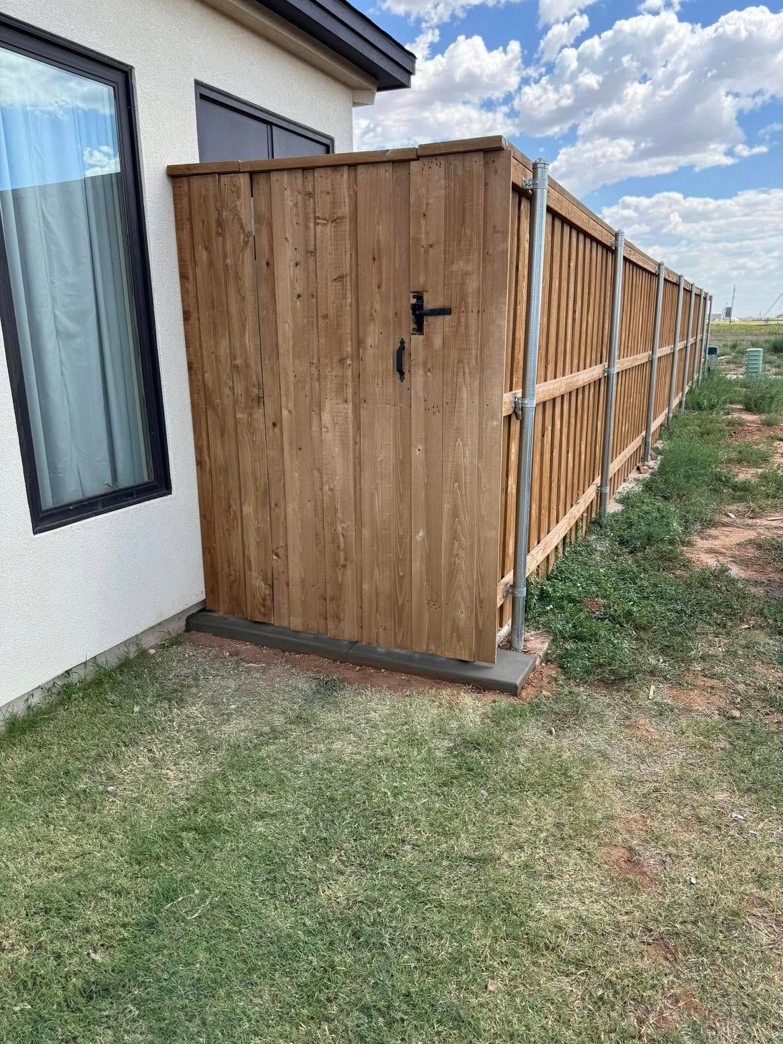 A wooden gate in a fenced yard, next to a house.