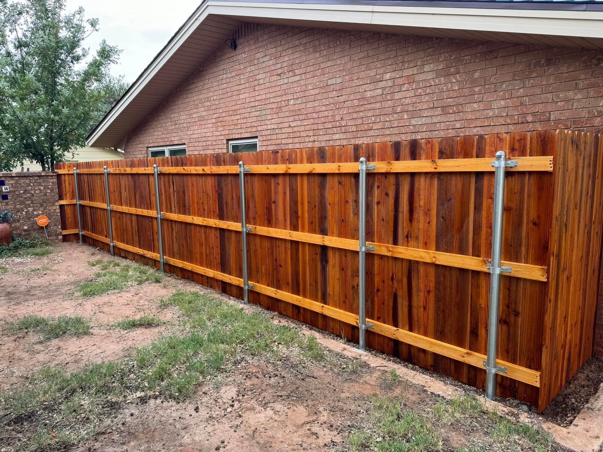Wooden fence with metal posts next to a brick building, in a yard.