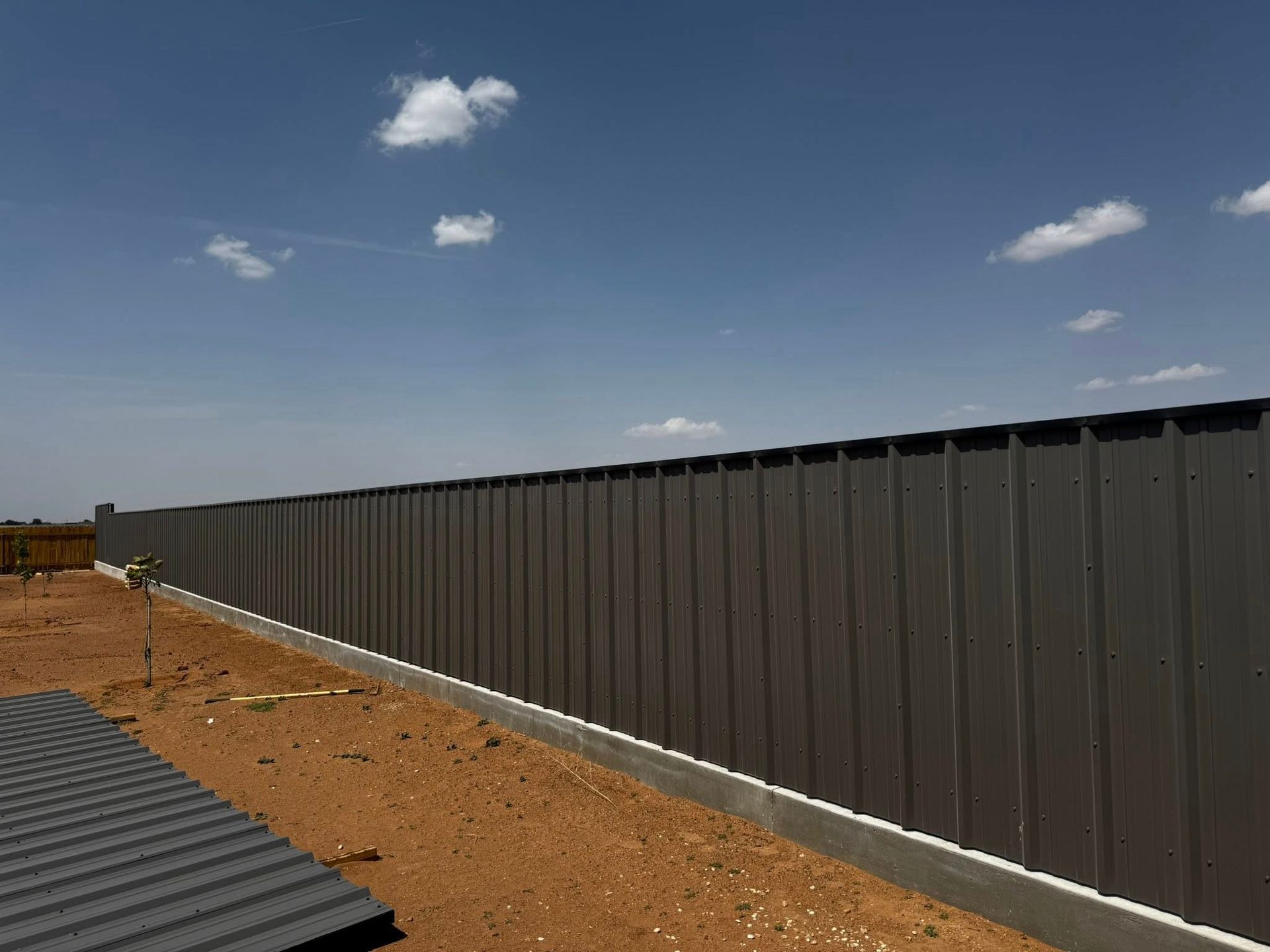 A gray metal fence extends across the frame under a blue sky with a few clouds.