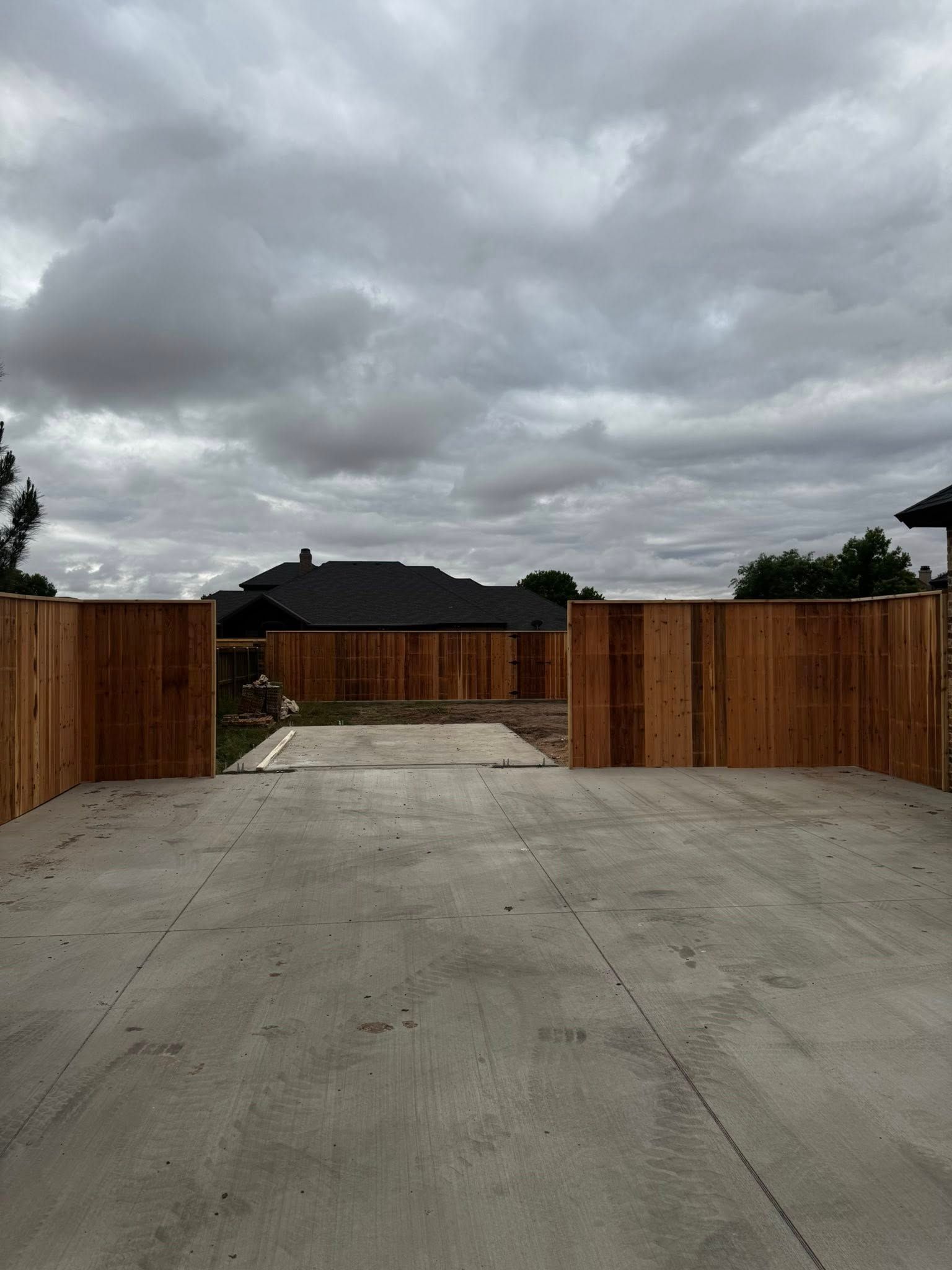 A concrete driveway with a wooden fence. The sky is overcast.