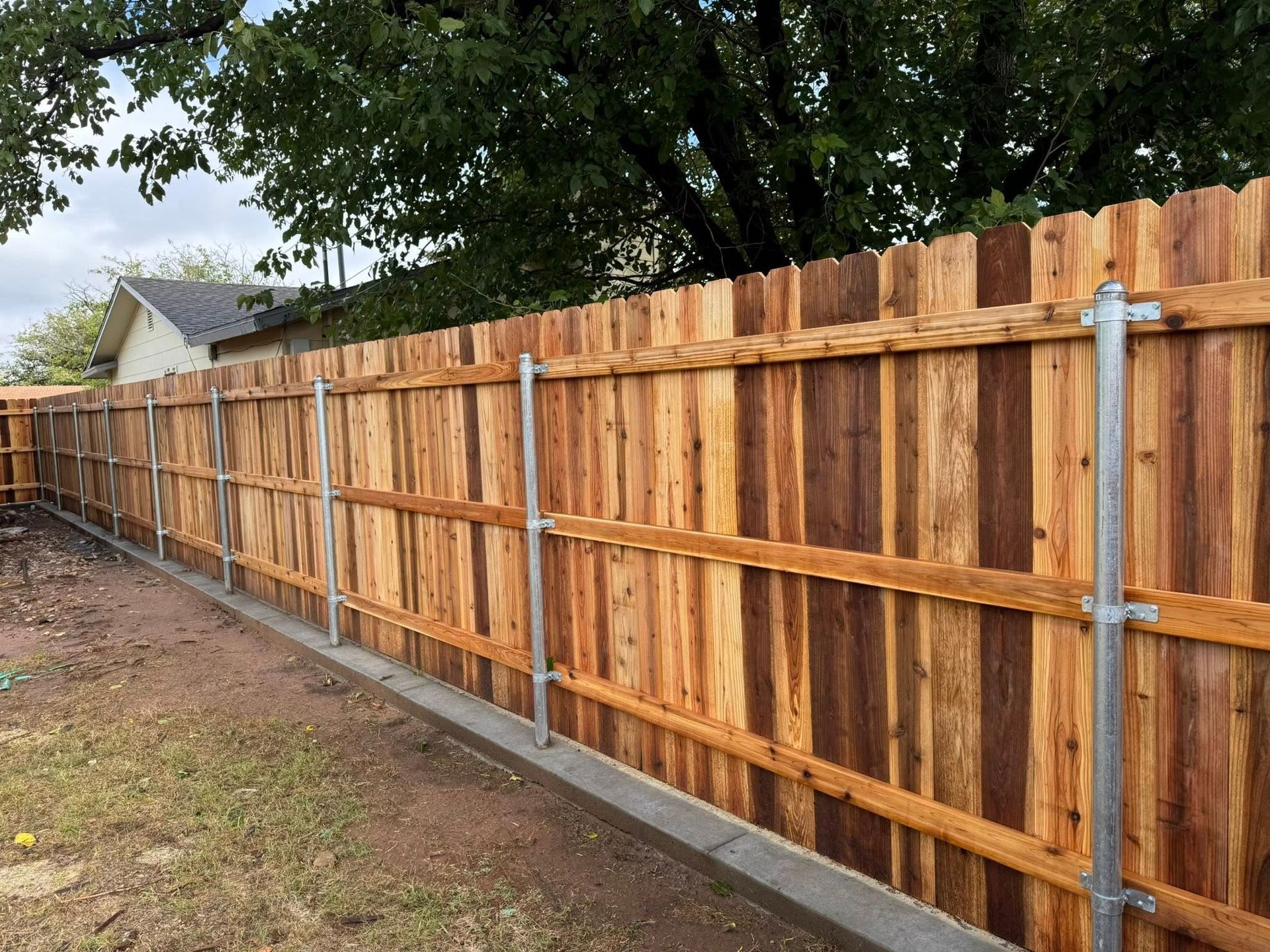 Wooden fence with metal posts, built along a concrete base in a yard.