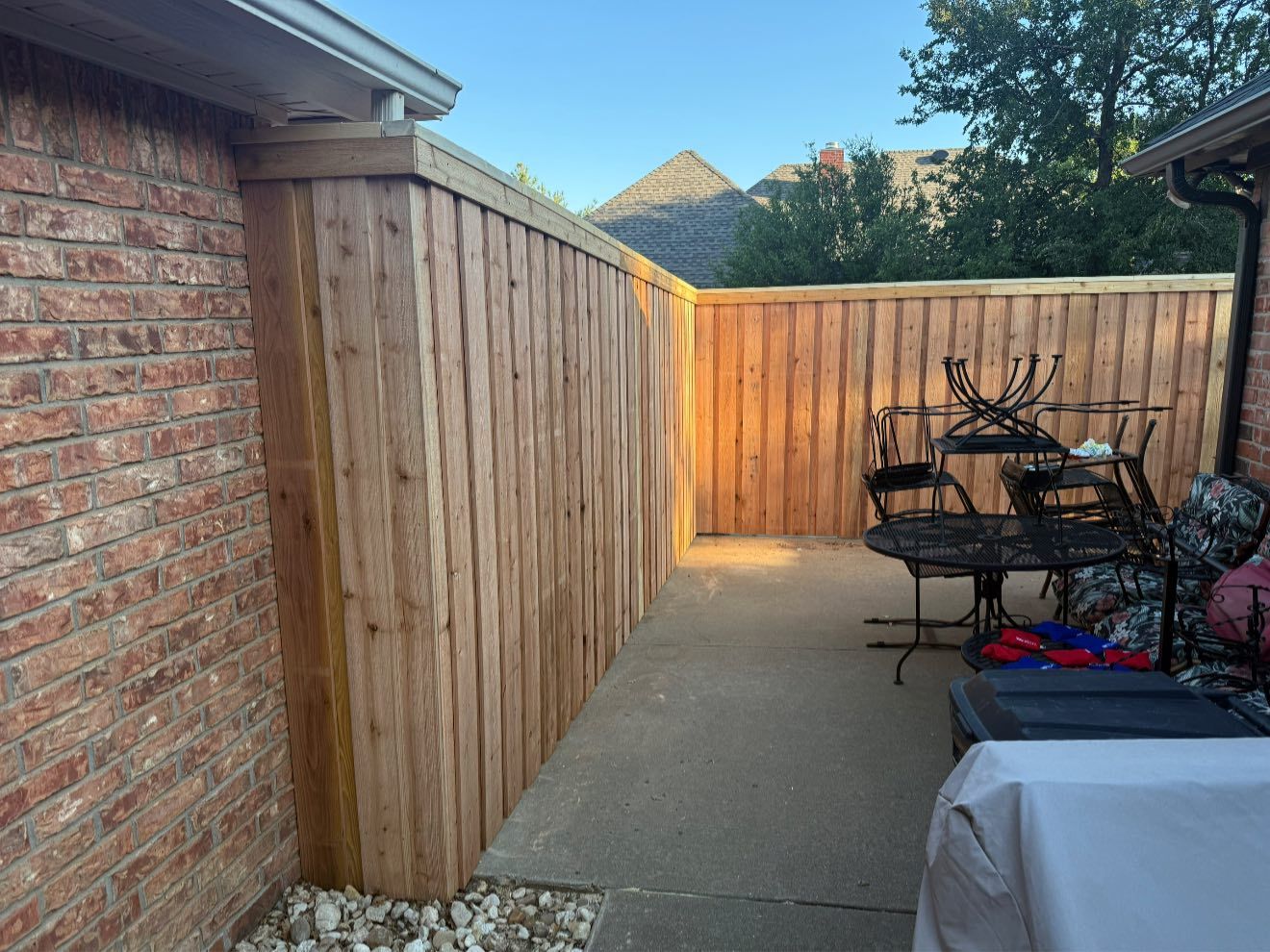 Wooden fence adjacent to a brick wall and concrete patio, with patio furniture visible.