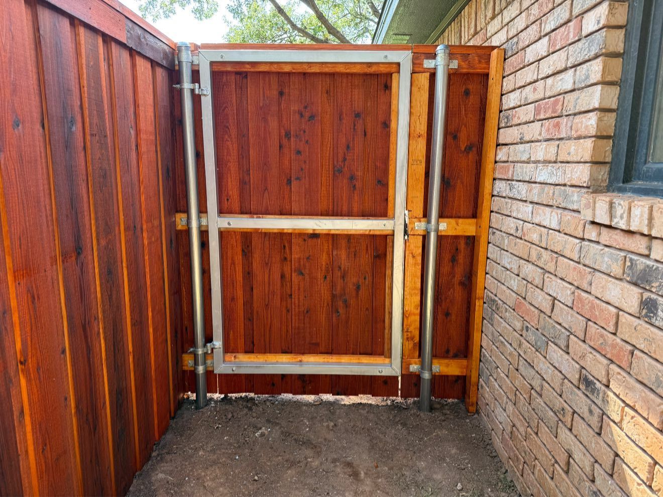 Wooden gate with metal frame set in a wooden fence next to a brick wall.