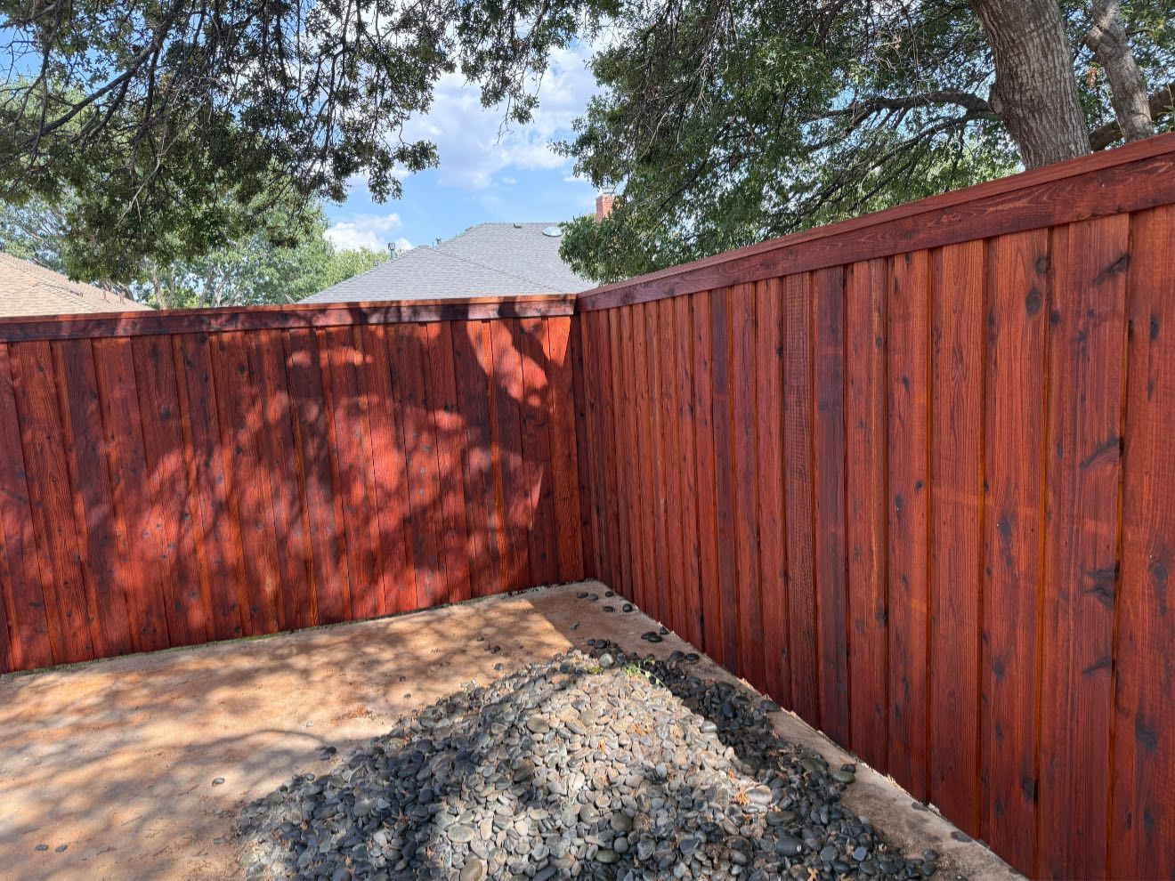 Red stained wooden fence surrounds a dirt area, sunny outdoors.
