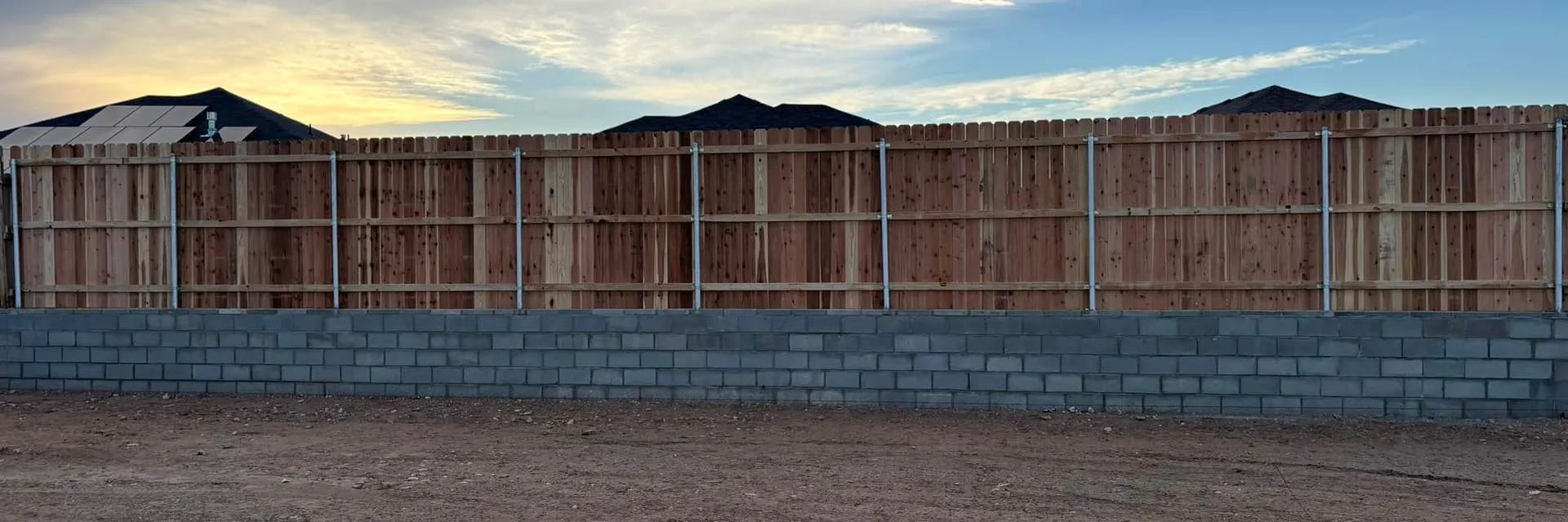 Wooden fence atop a brick wall against a twilight sky.