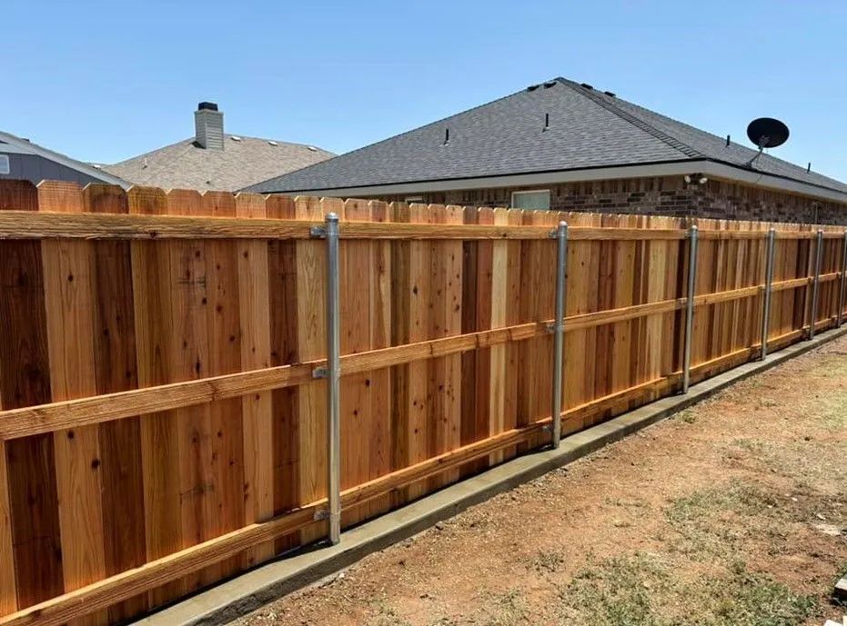 Wooden fence, stained brown, runs along a concrete border in a yard. Metal posts are spaced evenly.