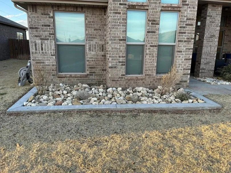 A brick home with a rock garden border in front, featuring dried plants and light-colored stones.