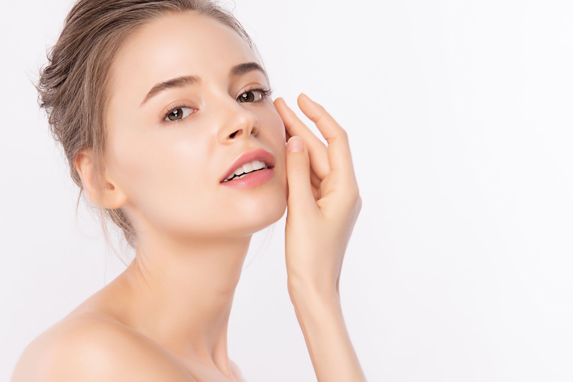 Woman touching her face, looking at the camera, with a neutral expression, against a white background.