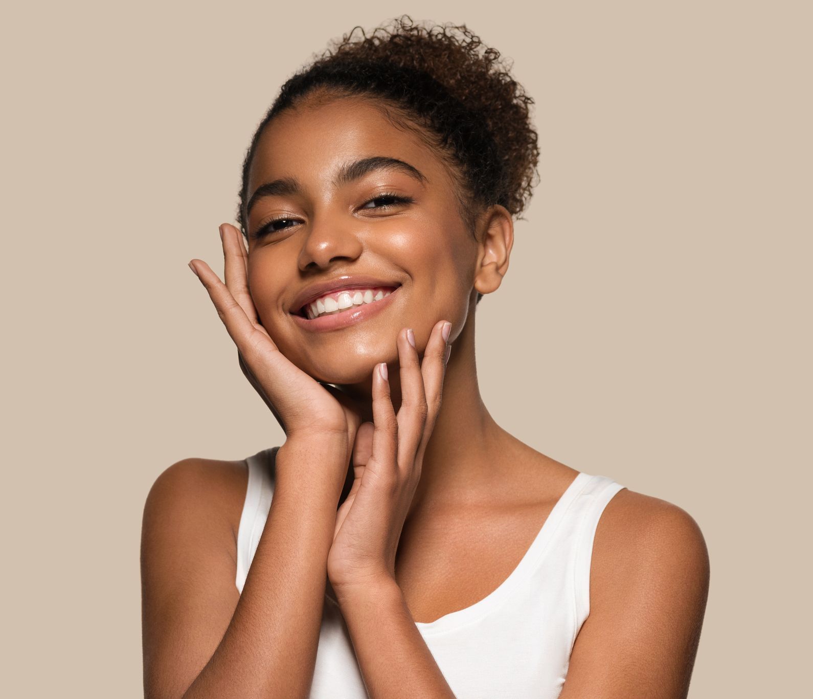 Woman smiling, touching face, wearing white top, against a beige background.