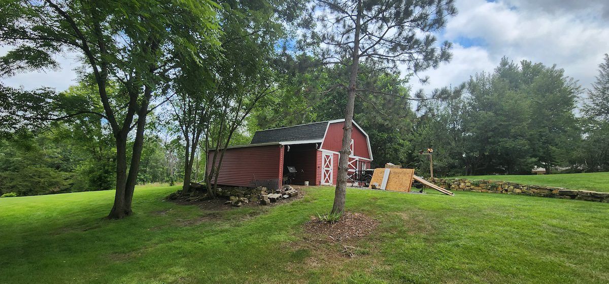A red barn is sitting in the middle of a grassy field surrounded by trees.