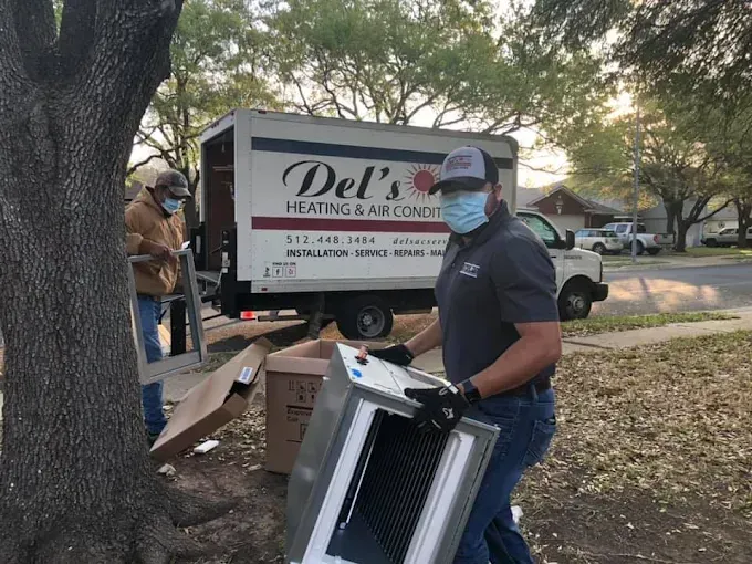 Two masked HVAC technicians installing air filter near a Del's Heating & Air Conditioning truck.