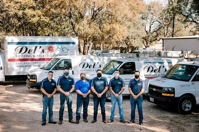 Team of men in blue shirts and masks standing in front of white service vans labeled 