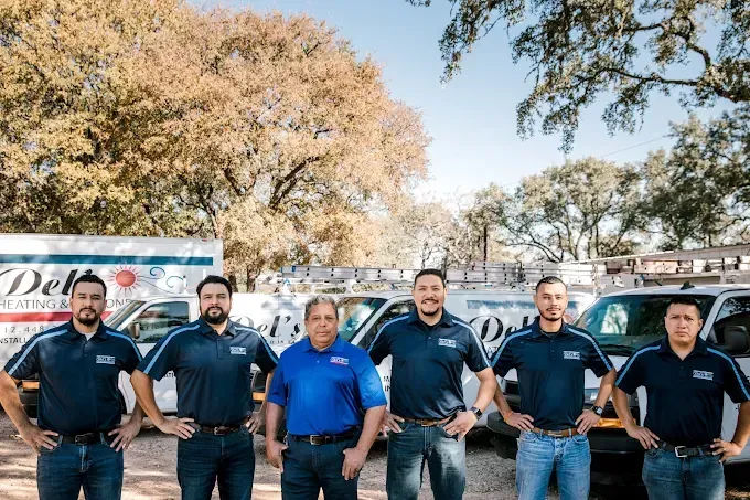 A group of men in front of service vans, smiling, hands on hips, under a tree.