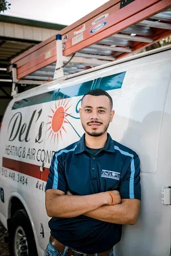 Man in blue polo shirt with arms crossed, standing in front of a Del's Heating & Air Conditioning van.