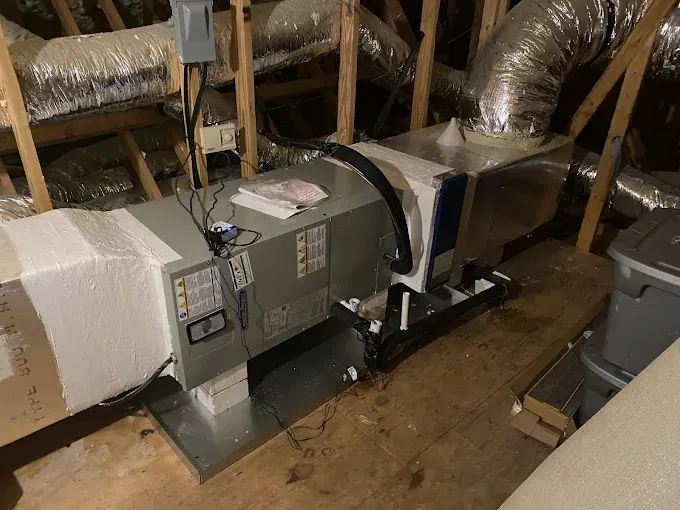 HVAC unit in an attic with ductwork, electrical connections, and insulation.