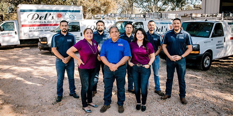 Group of people in front of Del's Heating & Air vans, all wearing company shirts.
