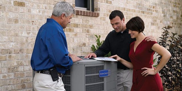 An HVAC technician reviews paperwork with a couple next to an outdoor air conditioning unit.