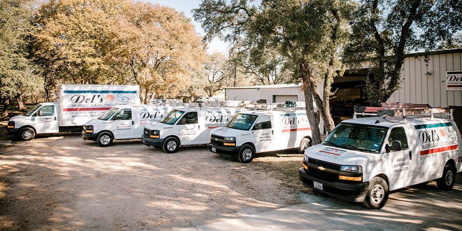 White service vans parked outside of a building, under trees. Company logos are visible.
